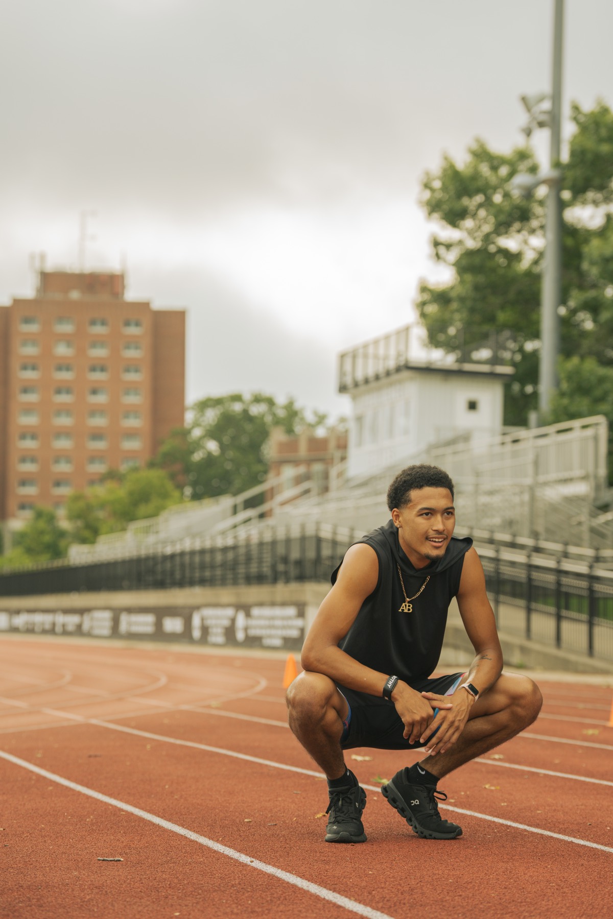 An athlete crouched on an outdoor track between reps, looking off camera
